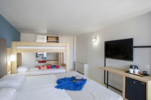 Una habitación de hotel con literas, un escritorio con televisor y una kitchenette pequeña.