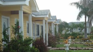 A row of yellow buildings with white trim and a landscaped garden with a statue. - Country Cove (Clarence Town)