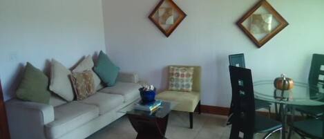 A living room with a sofa, a coffee table, a dining table with chairs, and two framed pictures on the wall.
