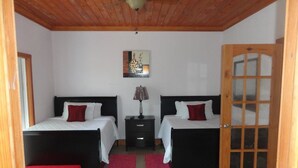 A bedroom with two beds, a wooden ceiling, a door with glass panels, and a small table with a lamp. - Country Cove (Clarence Town)