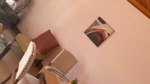 A room with a round glass table, a chair with a woven seat, a cushion, and a wall-mounted abstract painting. - Country Cove (Clarence Town)