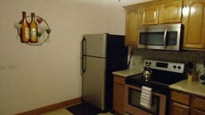 A compact kitchen with wooden cabinets, a stainless steel refrigerator, a microwave, and an oven. - Country Cove (Clarence Town)