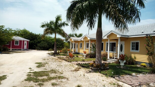 A row of yellow houses with a dirt road in front. - Country Cove (Clarence Town)