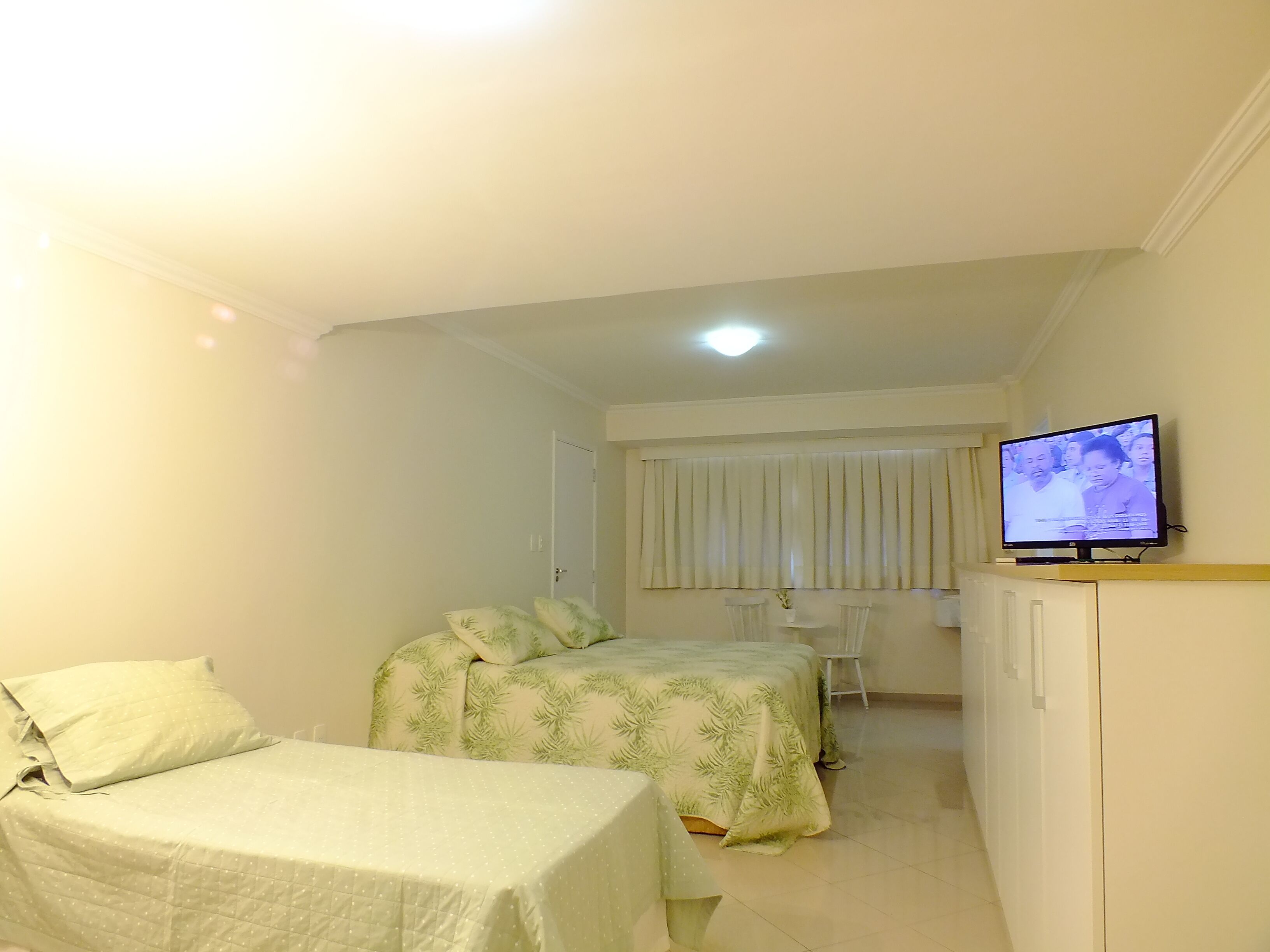 Una habitación pequeña y bien iluminada con dos camas, un televisor y una puerta que da a otra habitación.