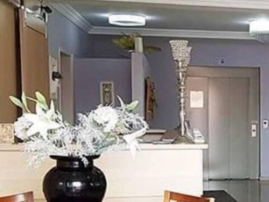 A reception area with a black vase of white flowers, a tall decorative lamp, and a closed door in the background.