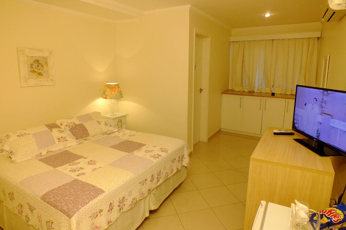 Een slaapkamer met een bed, een televisie, een lamp en een kleine kitchenette.