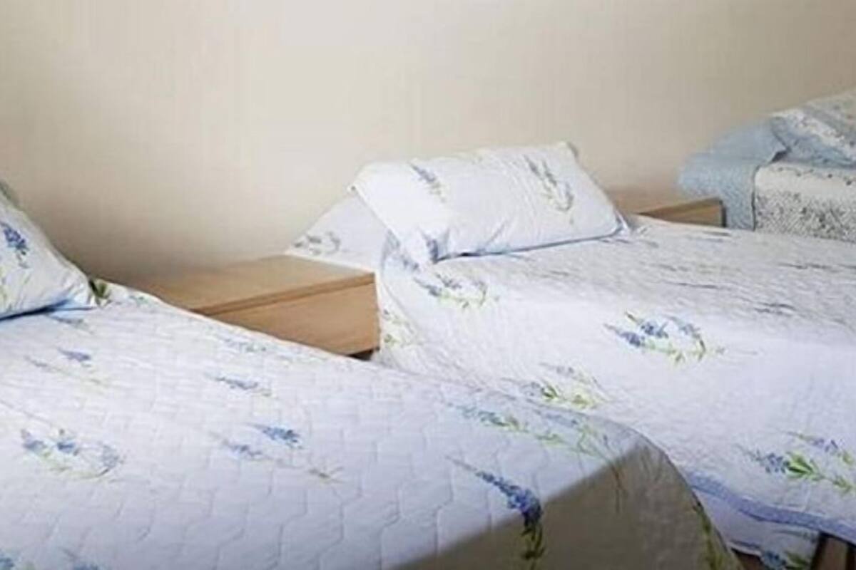 Twee eenpersoonsbedden met bloemenbeddengoed, houten hoofdborden en een effen muur op de achtergrond.