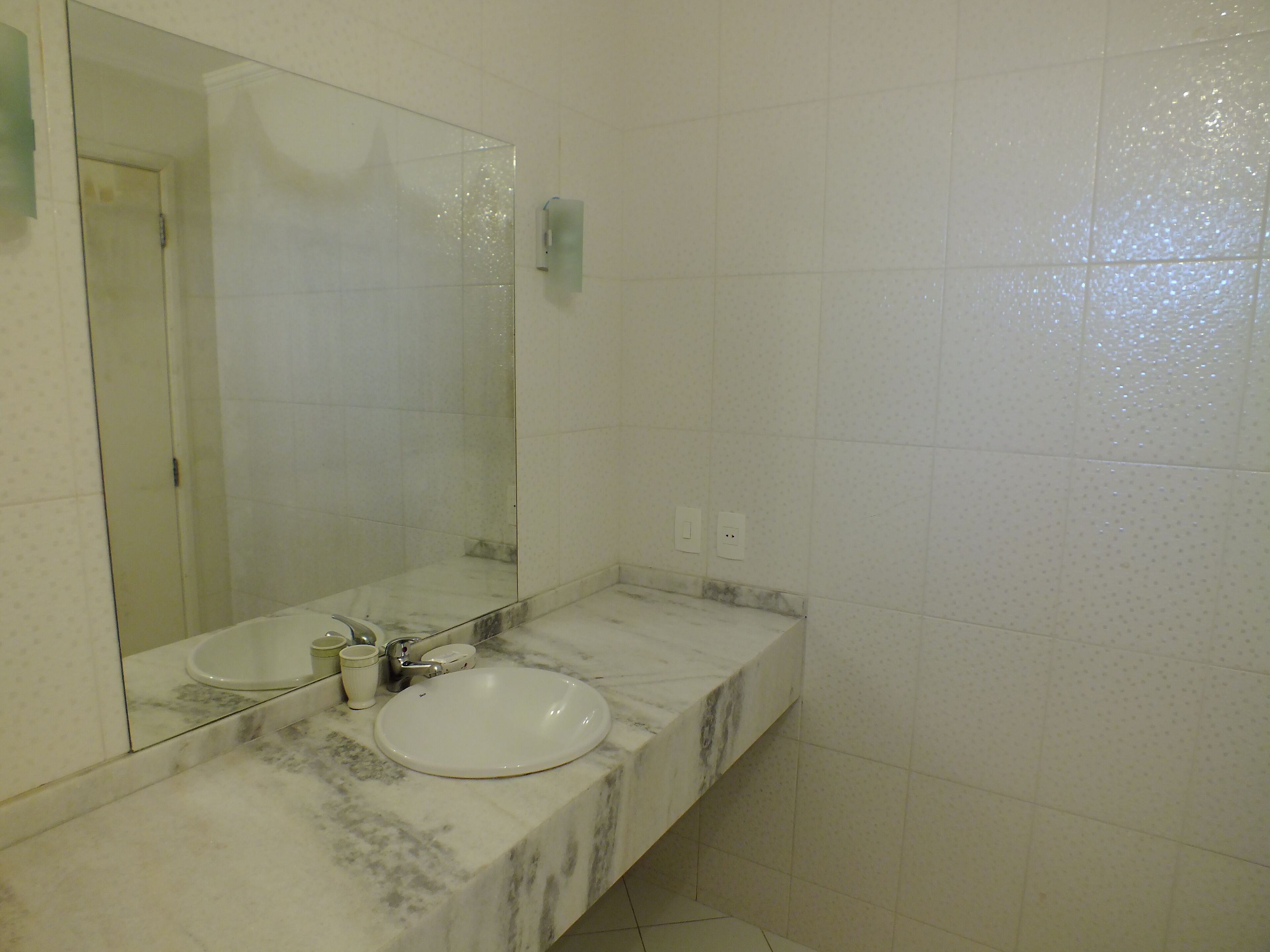 Un baño con lavamanos blanco, espejo y encimera de mármol.
