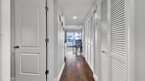 A narrow hallway with white doors and shutters, leading to a balcony with outdoor furniture.