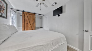 A bedroom with a bed, a ceiling fan, a TV mounted on the wall, and a wooden door. - Canal Views! Free Beach Service, Pet Friendly! Sandpiper Cove 4100! (Destin)