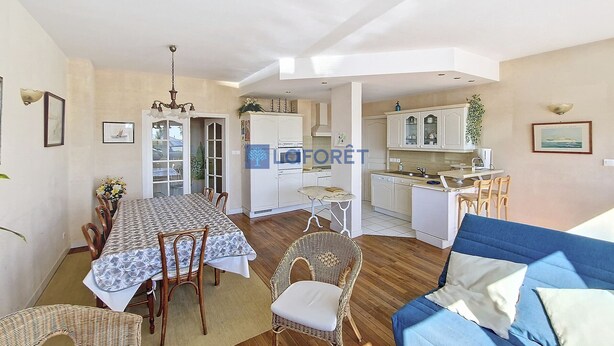 A spacious living area with a dining table, chairs, a blue sofa, and a kitchen in the background.