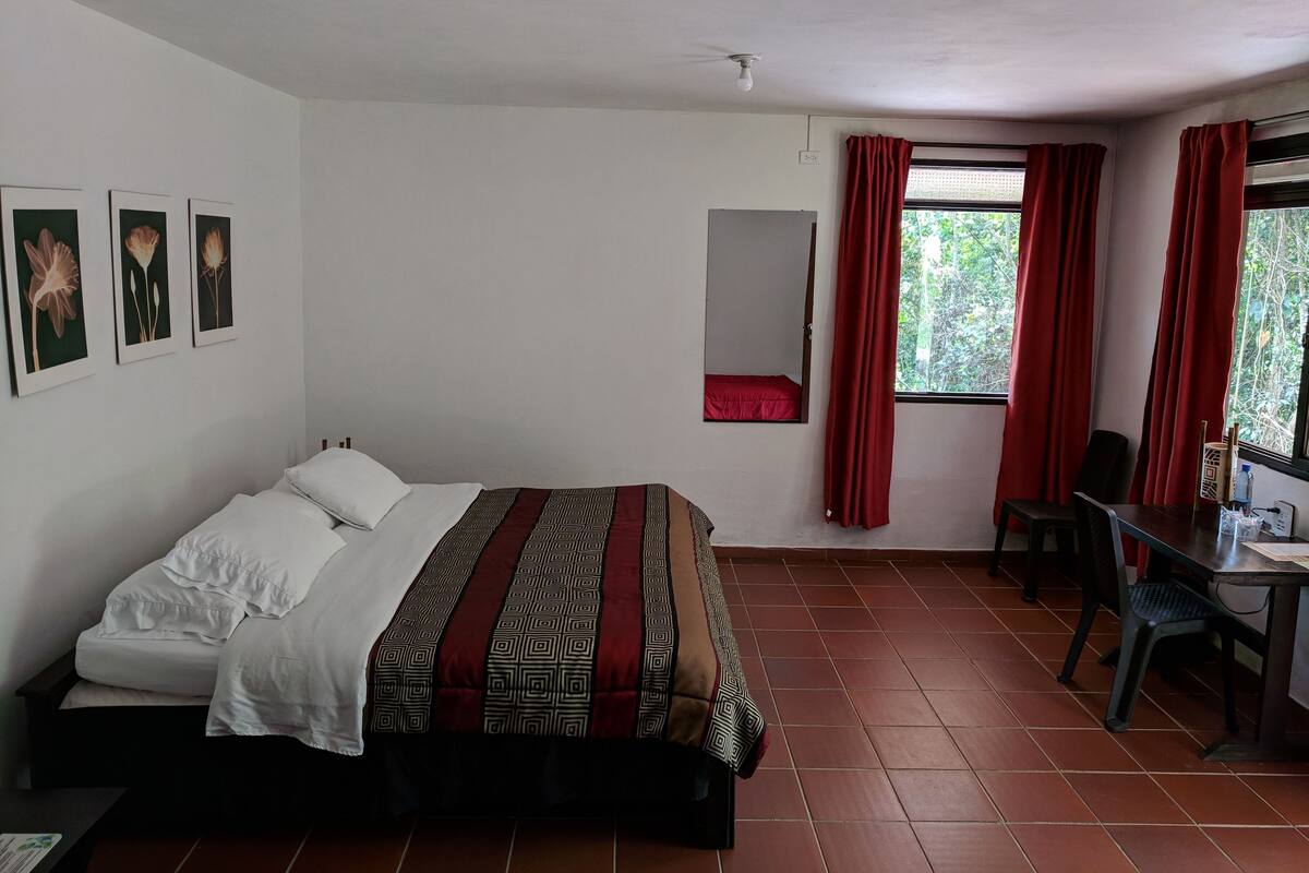 A bedroom with a bed, a desk, and a chair. There are three framed pictures on the wall.