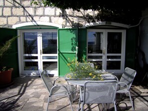 An outdoor patio with a table and chairs, a potted plant, and a green door. - newly renovated house, fantastic terrace with view of the sea (Dalmatien)
