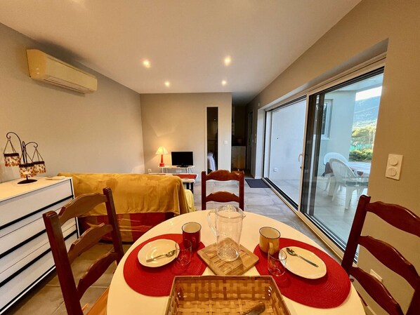 A dining area with a round table set for four, a television, and a bed in the background. - Appartement 2 pièces - 4 personnes - Cavalaire-sur-Mer (Cavalaire-sur-Mer)