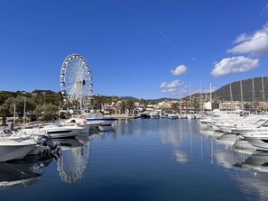 A marina with boats docked, a Ferris wheel, and buildings in the background. - Appartement 2 pièces - 4 personnes - Cavalaire-sur-Mer (Cavalaire-sur-Mer)