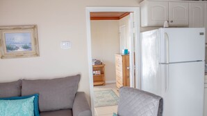 Een woonkamer met een grijze bank, een witte koelkast en een houten kast.