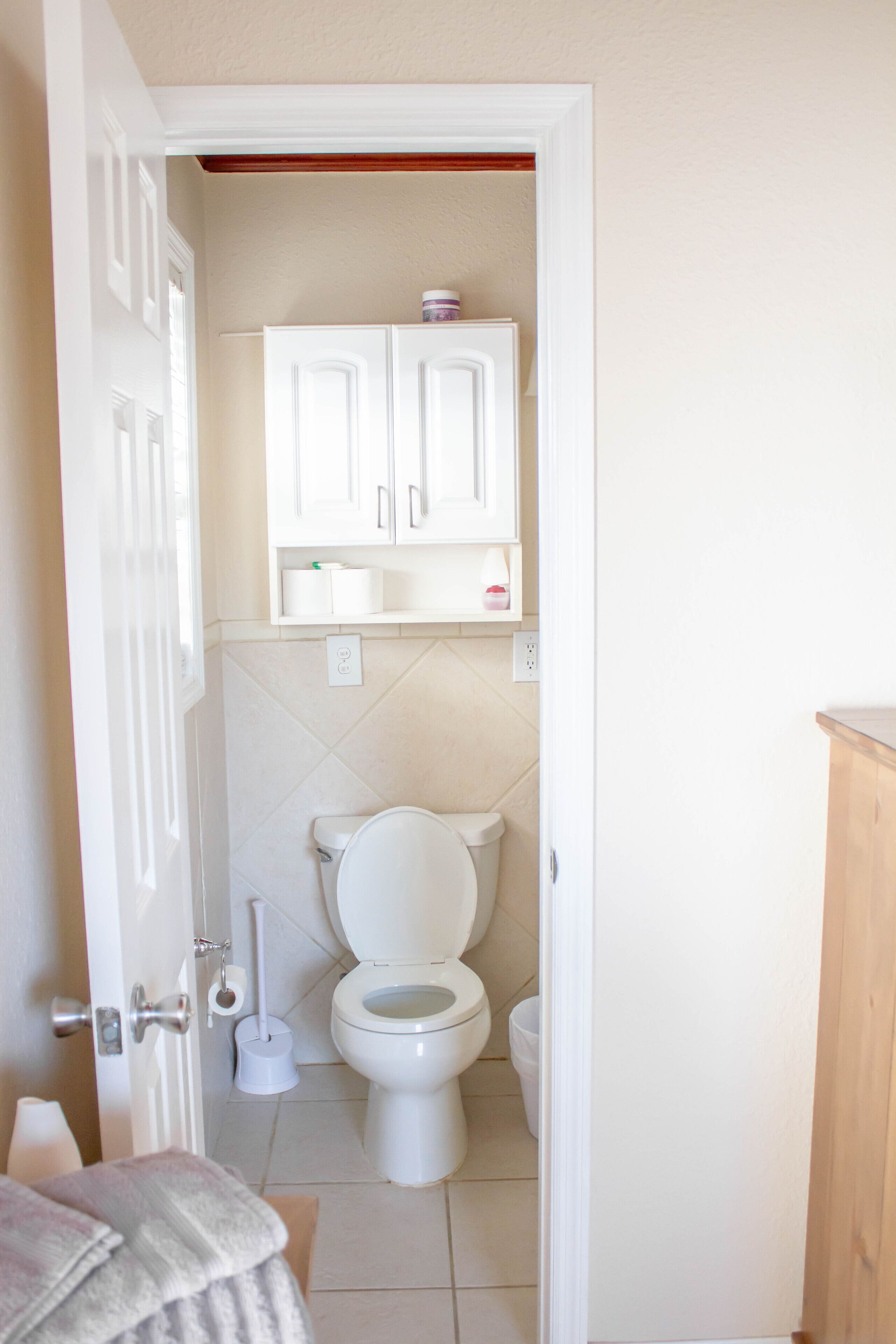 A bathroom with a toilet, a cabinet above the toilet, and a towel rack.