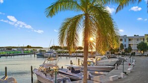 A marina with boats docked, a palm tree, and a building in the background. -  Mariner's Club 606 • Clean & Reliable 4/4 • Amazing Pools & Resort Amenities (Key Largo)