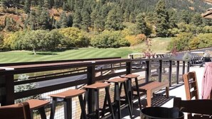 Een restaurantterras met tafels en stoelen, met uitzicht op een bergachtig landschap en een golfbaan.
