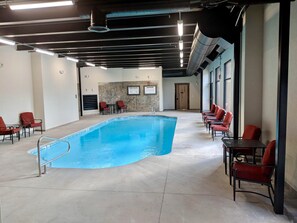A swimming pool with red chairs and tables, a stone wall, and a door in the background.