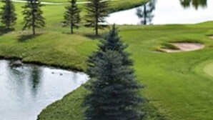 Een golfbaan met een vijver, omringd door bomen en bergen op de achtergrond.
