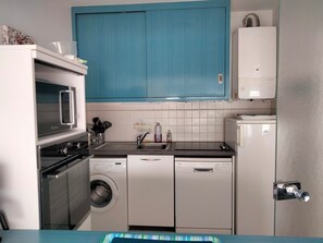 A compact kitchen with a washing machine, dishwasher, microwave, and a small refrigerator.
