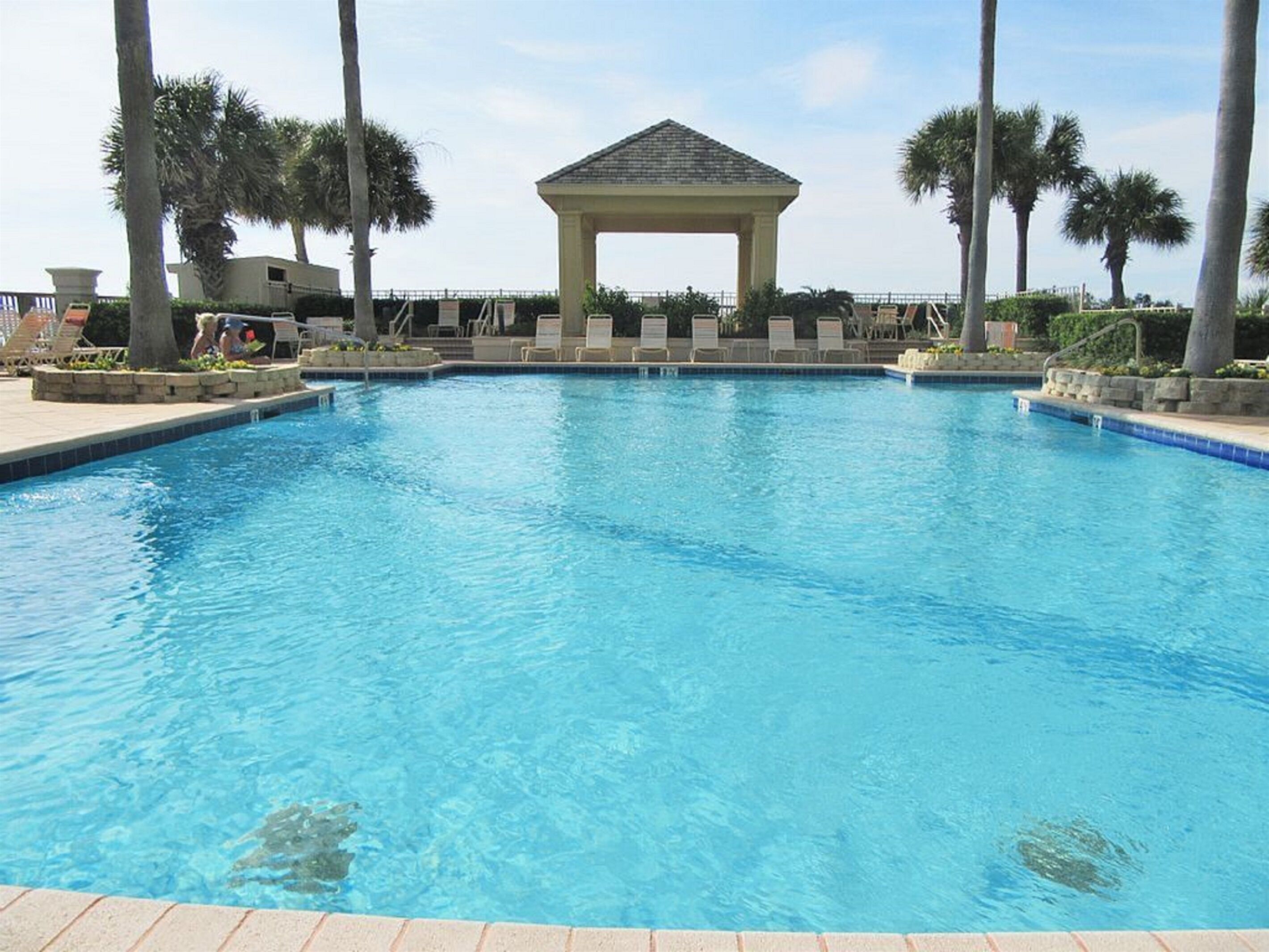 A swimming pool with lounge chairs and a gazebo.