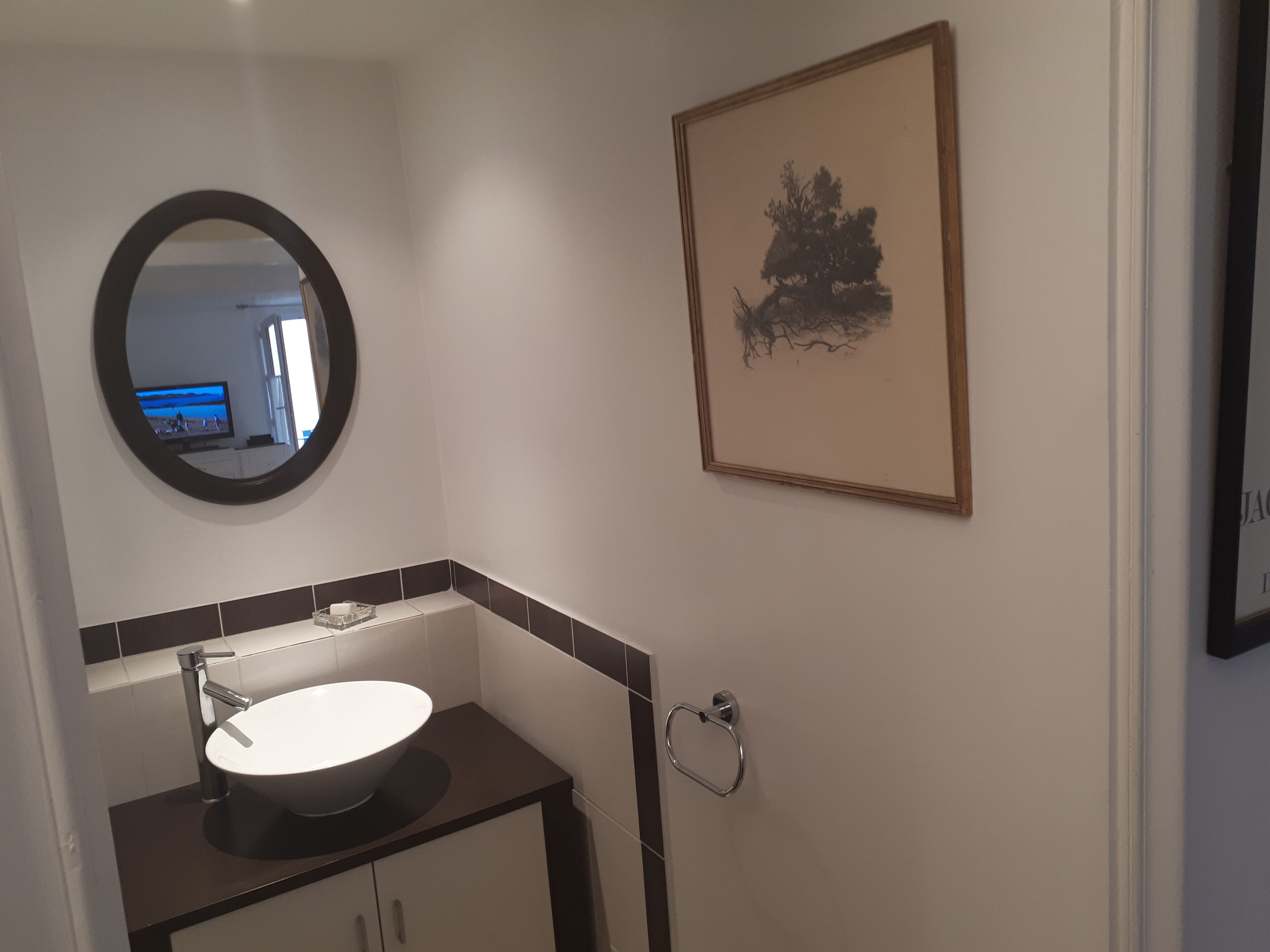A bathroom with a round mirror, a sink, and a framed artwork on the wall.