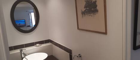 A bathroom with a round mirror, a sink, and a framed artwork on the wall.