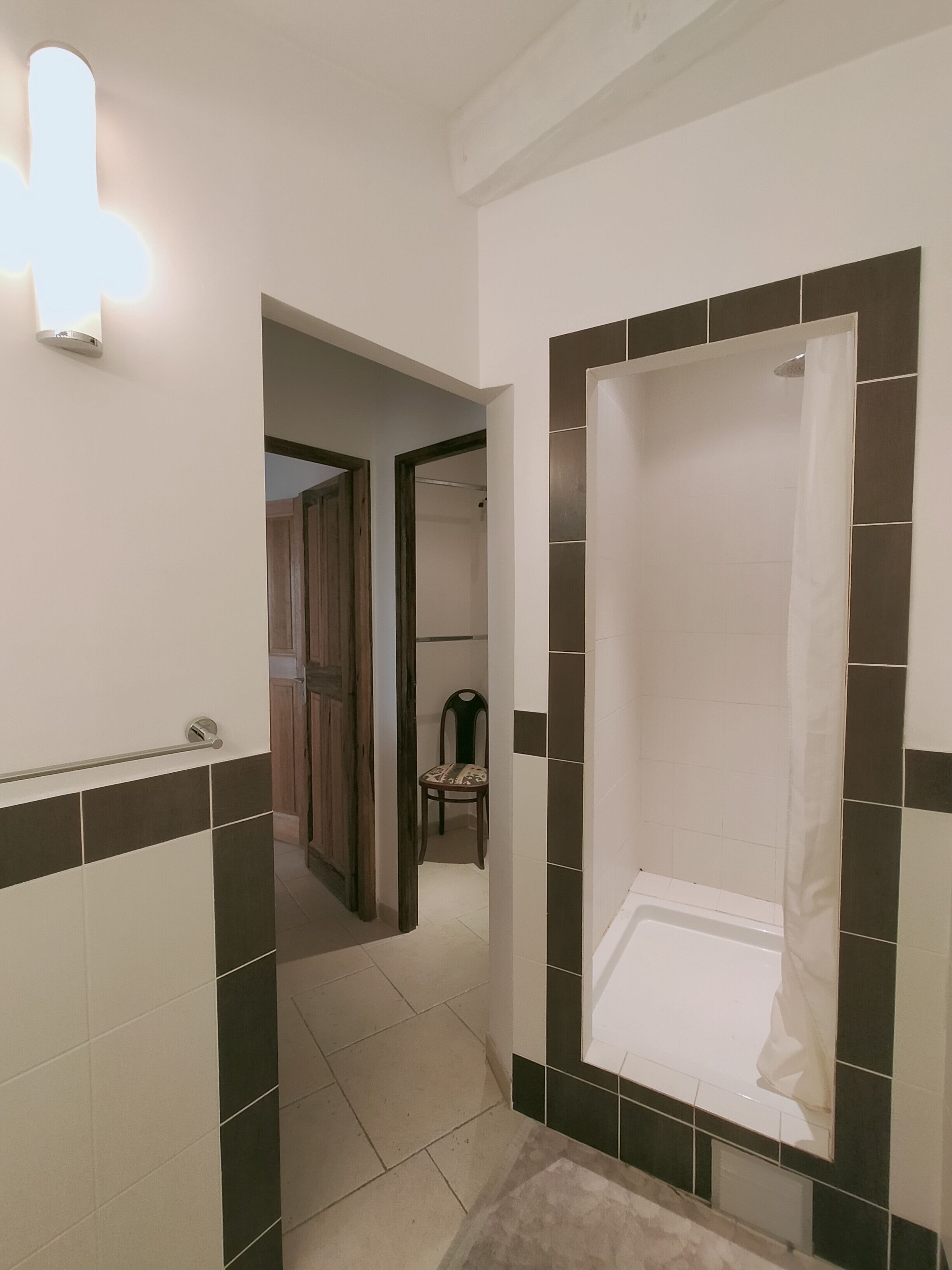 Une salle de bain avec une douche, des murs carrelés et une chaise au fond.