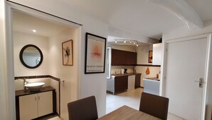 Een moderne keuken met donkere kastjes, een wit aanrechtblad en een spoelbak. Er hangt een lijst met kunst aan de muur en op de eettafel staat een turquoise kom.