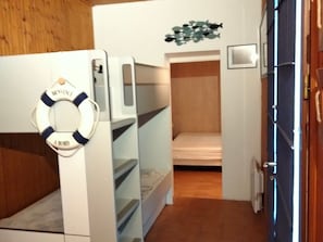 A bunk bed room with a life preserver decoration, a small shelf, and a wooden door.