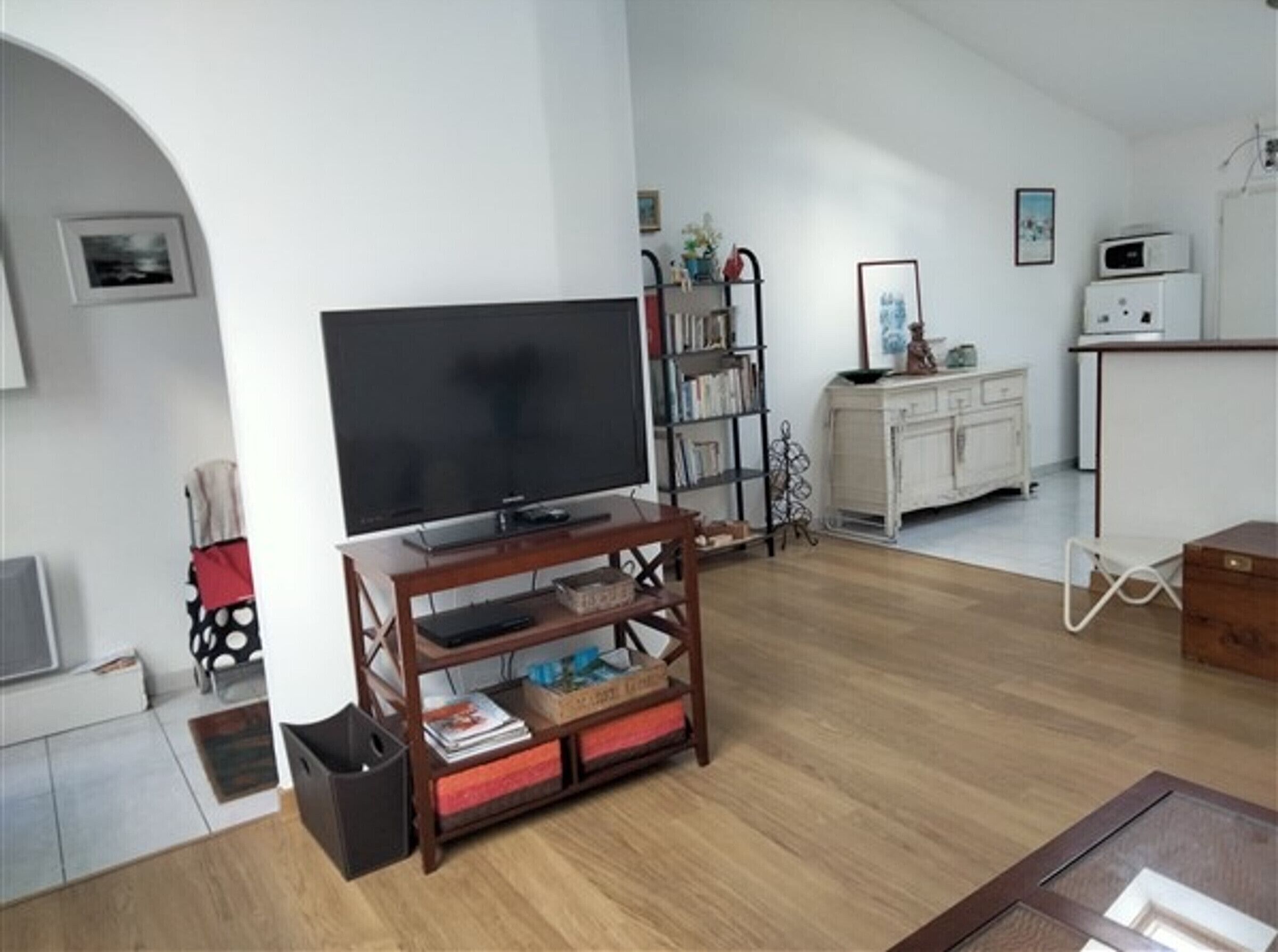 Ein Wohnzimmer mit einem Flachbildfernseher auf einem Holzboden, einem Bücherregal, einem weißen Schrank und einer Mikrowelle.