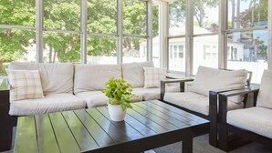 A modern living room with a sofa, a coffee table, and a chair. There are large windows providing a view of trees and buildings outside.