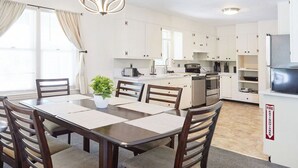 A modern kitchen with white cabinets, a dining area with a wooden table and chairs, and a pendant light.