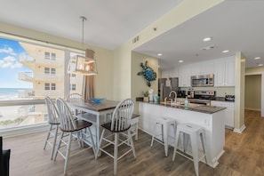 Una cocina moderna con armarios blancos, una isla grande con taburetes y vistas al océano.