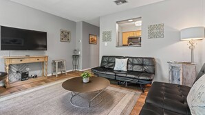 A modern living room with a leather sofa, a coffee table, a TV, and a kitchen area visible through an open doorway. - Captain's Quarters Riverfront #1 (Nashville)