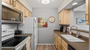 A compact kitchen with a stove, oven, microwave, refrigerator, sink, and wooden cabinets. - Captain's Quarters Riverfront #1 (Nashville)