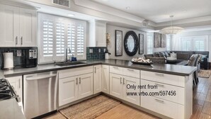 A modern kitchen with white cabinetry, a large island, and a dining area with a sofa. - Newly built + Ocean View + Steps to Sand (Newport Beach)