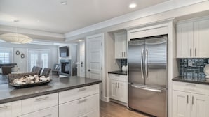 A modern kitchen with white cabinetry, stainless steel appliances, and a large island with a bowl of mushrooms. - Newly built + Ocean View + Steps to Sand (Newport Beach)