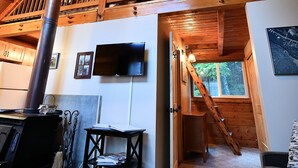 Un intérieur rustique avec un plafond en bois, un téléviseur fixé au mur et un escalier menant à un niveau supérieur.