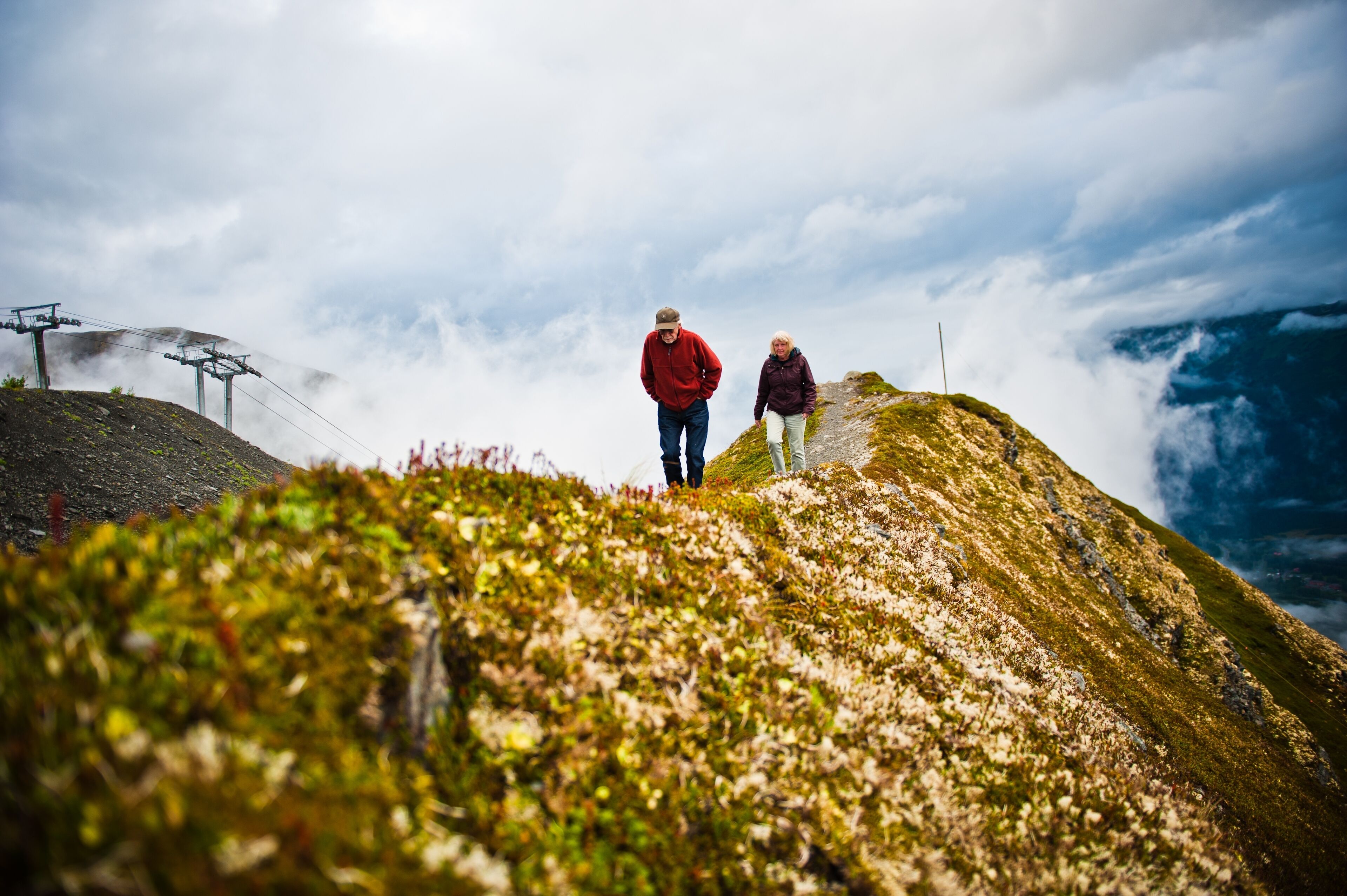 Two people standing on a grassy hill with a ski lift in the background.