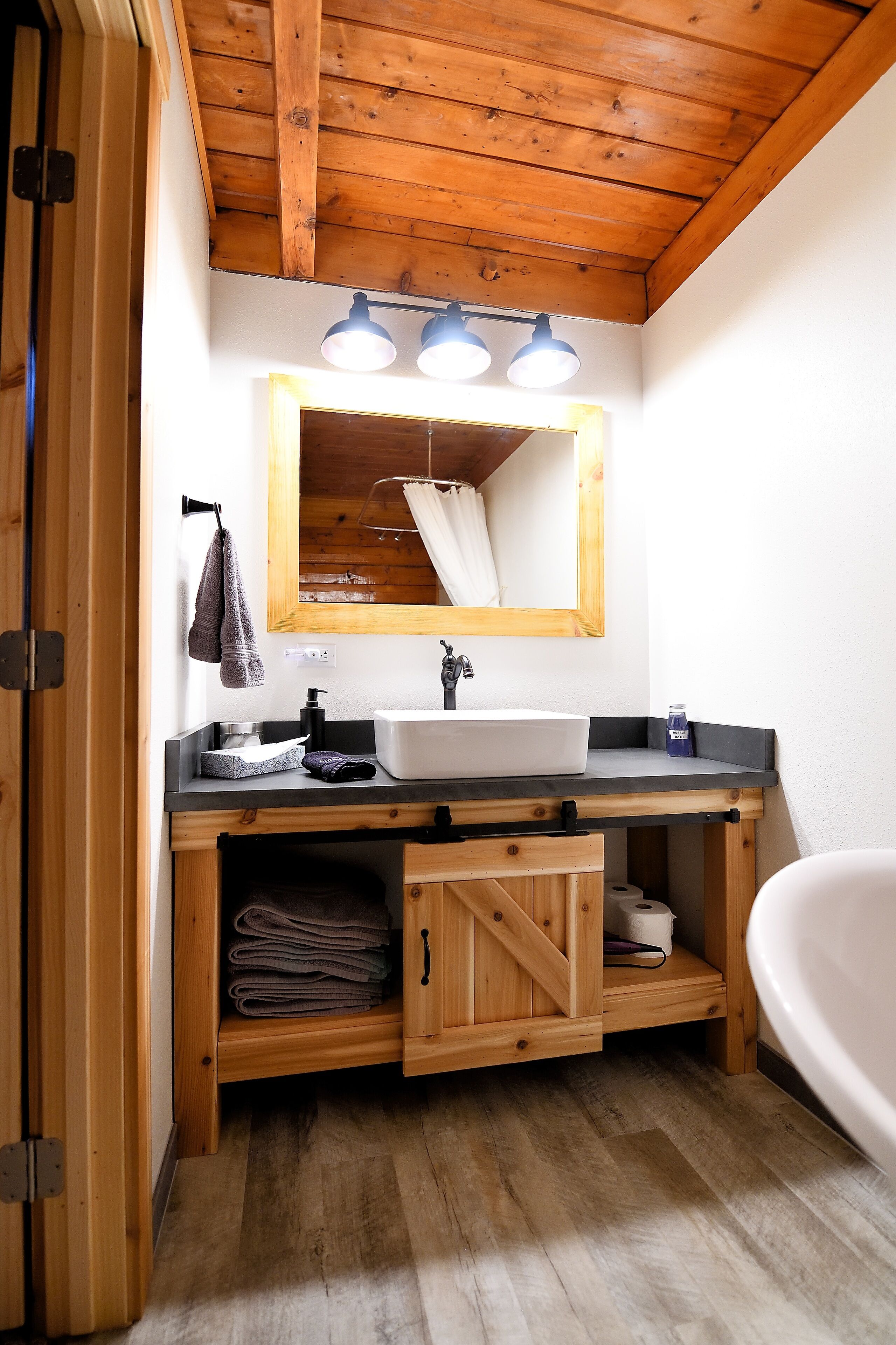 A bathroom with a wooden ceiling, a sink with a mirror above it, and a bathtub.