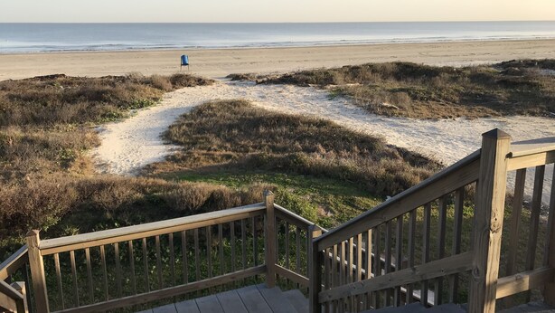 A wooden staircase leading to a beach with a sandy path and grassy dunes.