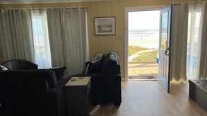 A living room with a sofa, a small table, and a door leading to a balcony with a view of the beach.