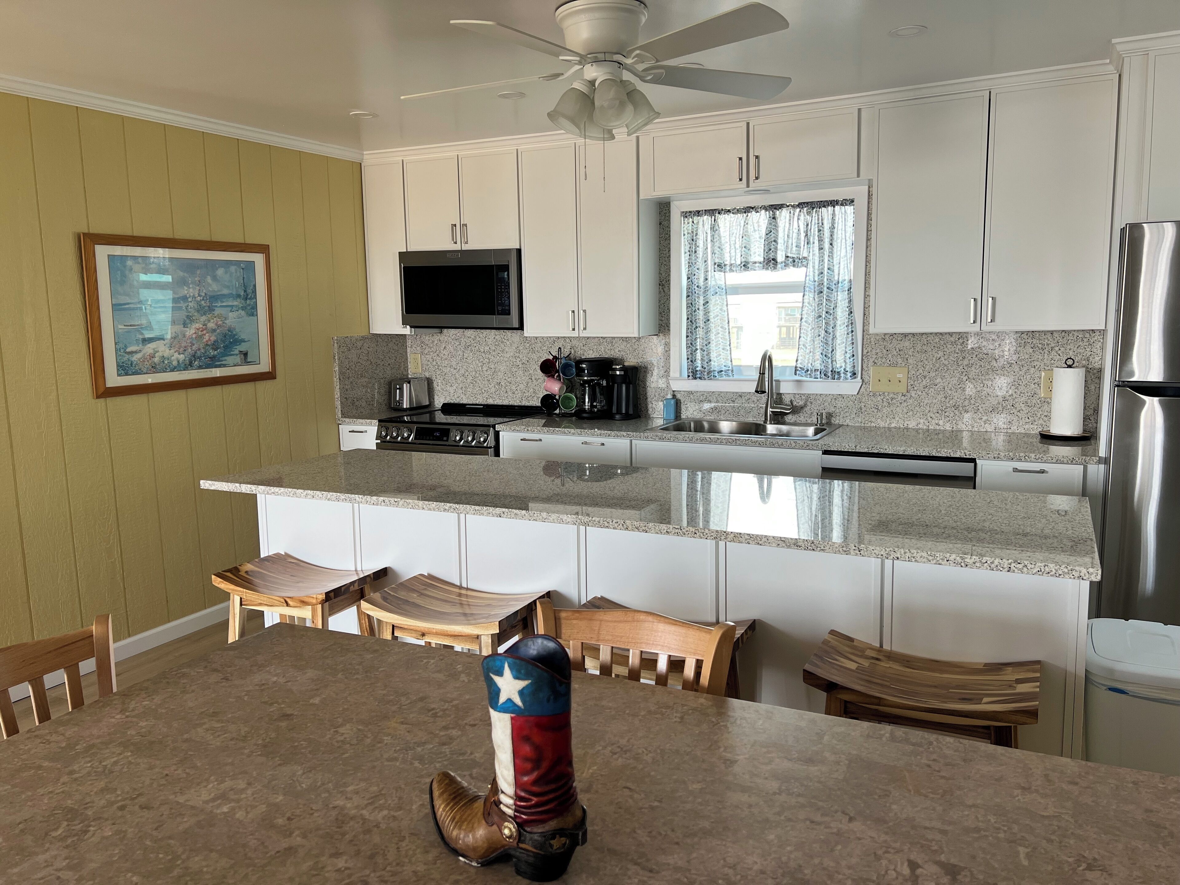 A kitchen with white cabinets, a granite countertop, a microwave, a stove, and a ceiling fan.