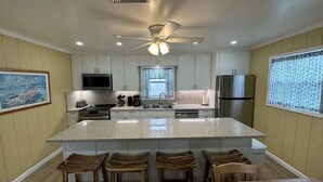 A modern kitchen with a central island, wooden bar stools, stainless steel appliances, and a ceiling fan.