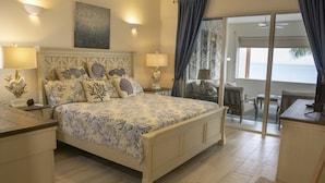 A bedroom with a large bed, two bedside tables, and a view of the sea through a sliding glass door.