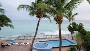 A pool area with lounge chairs, a hot tub, and a view of the ocean.