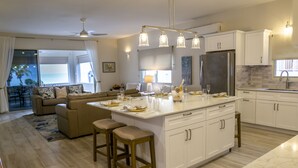 A modern kitchen with white cabinetry, a central island, and a dining area with a view of the ocean.